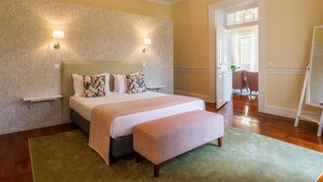 Un dormitorio con una cama grande, dos lámparas de noche, un banco y una puerta que da a otra habitación.