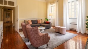 Un salón espacioso con un sofá gris, sillones estampados y otomanas sobre piso de madera.