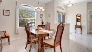 Uma sala de jantar com mesa e cadeiras de madeira, um candelabro e uma janela com persianas.
