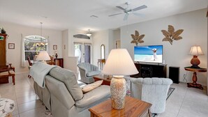 Uma sala de estar ampla com um sofá cinzento, uma mesa de centro de madeira e uma televisão exibindo uma cena de praia.