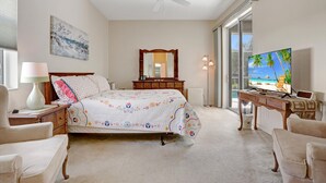 Quarto com cama, cômoda, televisão, ventilador de teto e uma grande janela.