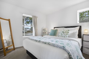 A bedroom with a bed, a window, a ladder, and a bedside table.
