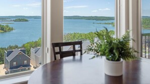 A dining area with a table and chairs, overlooking a lake with houses and greenery in the background. - Spacious, Family Friendly Condo with Lake View - The Majestic at Table Rock (Branson)