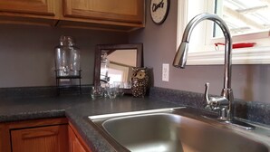 A kitchen with a stainless steel sink, wooden cabinets, and a window with blinds. - Quiet Barn Loft at Rock'n'Rose (Morganton)