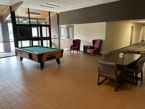 Una mesa de billar en una sala con pared de ladrillo, una mesa de pool y una zona de estar con sillas.