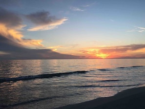 Ein Sonnenuntergang über einem ruhigen Meer, sanfte Wellen umspülen den Strand.