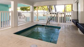 Una piscina interna con pavimento piastrellato, una scaletta e un recinto bianco tutt'intorno.