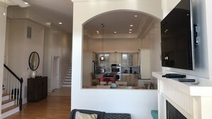Un vaste espace de vie doté d’une cheminée, d’un téléviseur fixé au mur et d’une cuisine ouverte sur le salon par une arche.