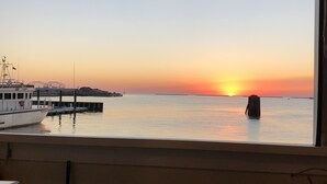Une vue sur le coucher de soleil, prise depuis une fenêtre donnant sur une mer calme, avec un quai et un bateau.
