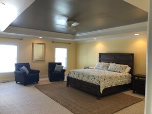Ein Schlafzimmer mit einem großen Bett, zwei Sesseln, einem Deckenventilator und zwei Fenstern.