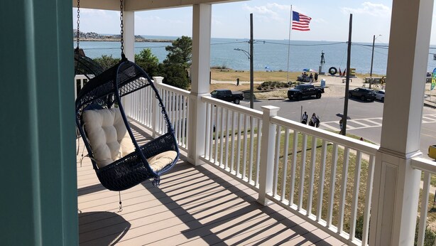 Une véranda avec un fauteuil suspendu, une vue sur la plage et un drapeau américain.