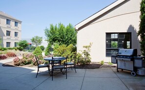 A patio with a table and chairs, a grill, and a building in the background. - Free Breakfast Pool & Hot Tub. Near East Towne Mall! (Madison)