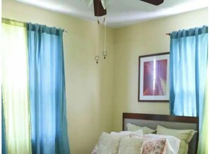 Cozy retreat with a bed positioned against a wall, flanked by two windows and a ceiling fan above.