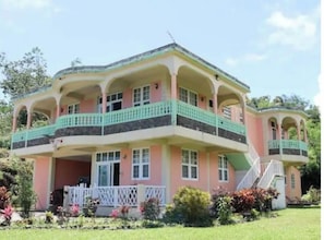 A two-story building with a balcony on the upper floor, surrounded by greenery.