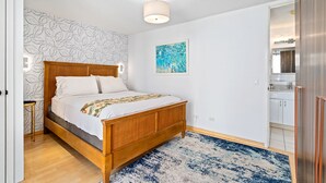 Et soveværelse med en træseng, et blåt og hvidt tæppe med et mønster, en væg med bladmotiv og en loftlampe.