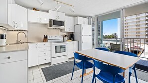 Et moderne køkken med hvide skabe, en mikrobølgeovn, ovn og et spiseområde med blå stole og et hvidt bord.