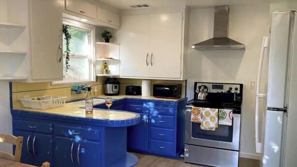 Una cocina moderna con armarios blancos, una isla azul, electrodomésticos de acero inoxidable y una ventana con una planta.