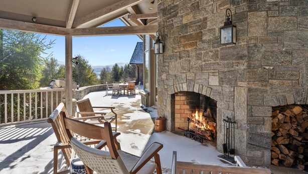 Une cheminée en pierre avec un feu de bois, des chaises en bois et une terrasse enneigée.