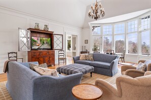 A spacious living room with a large television, comfortable seating, and a view through large windows. - Elegant Mountain Home with Views (Banner Elk)