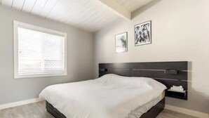 Un dormitorio con una cama, una ventana con persianas y dos cuadros en la pared.