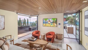 Una sala de estar moderna con techo de madera, un ventanal con vistas a cactus y una playa, y un cuadro de colores en la pared.