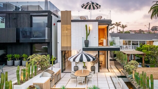 Una casa moderna con patio, mobiliario exterior y diversos cactus.