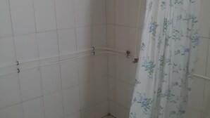 A shower area with white tiled walls, a shower curtain with a floral pattern, and a handheld showerhead.