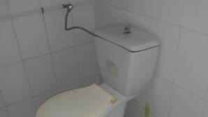 A standard white toilet with a green plunger beside it in a bathroom with white tiled walls and floor.