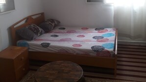 A bedroom with a bed, a small round table, a window with curtains, and a patterned rug.