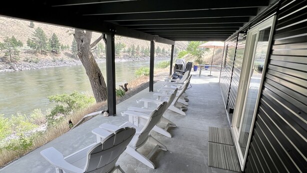 Un espacio de estar al aire libre techado con sillas blancas y vista al río.