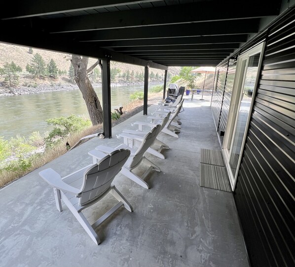 A covered outdoor seating area with white chairs and a view of a river.