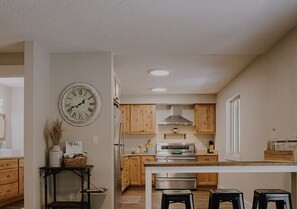 A modern kitchen with wooden cabinets, a stainless steel refrigerator, and a central island with stools.