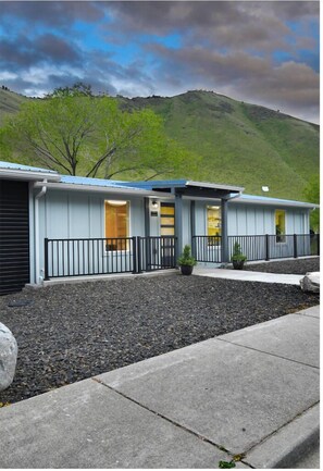 A modern motel with a flat roof, a covered outdoor area, and a view of a green hill in the background.