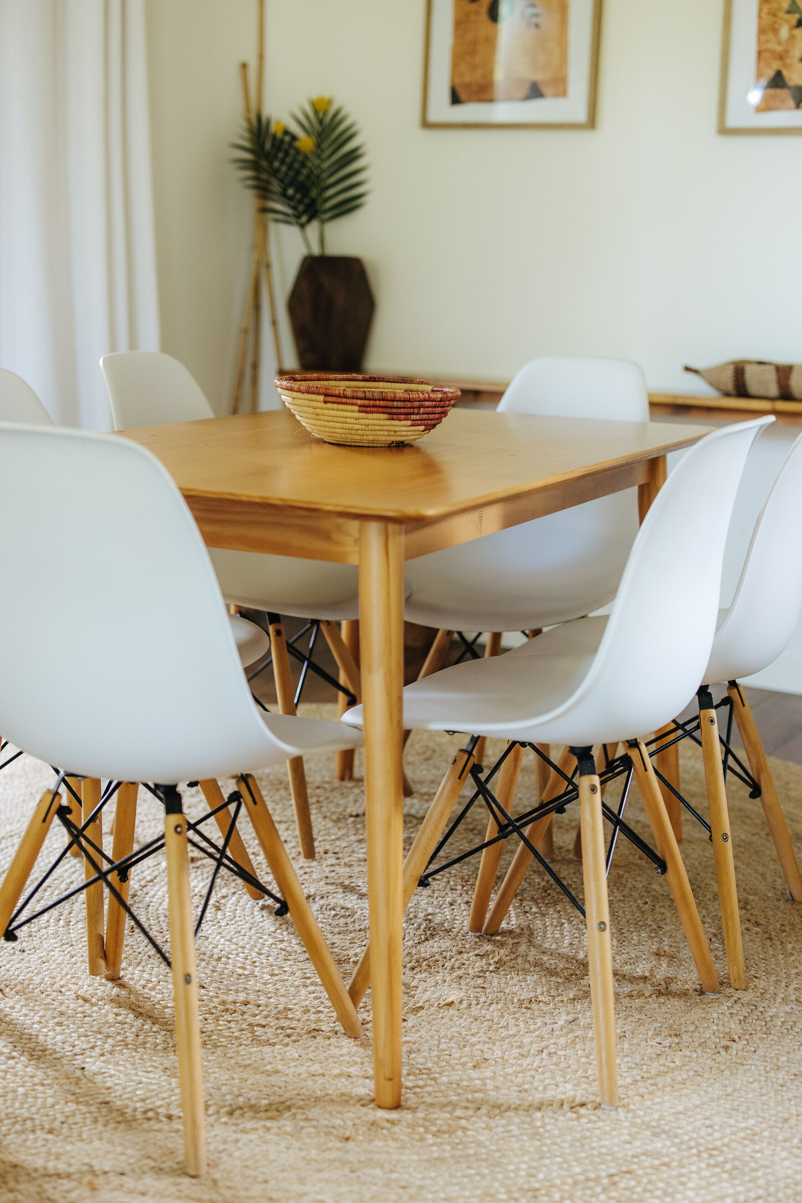 Un coin repas avec une table en bois, des chaises blanches et un panier tressé posé sur la table.