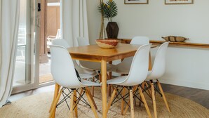 Ein Essbereich mit Holztisch, weißen Stühlen, einem gewebten Teppich und einer Deckenleuchte.
