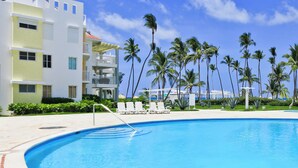 A modern hotel with a swimming pool, palm trees, and a clear blue sky. - Playa Turquesa I-202 Premier Beachfront Ocean View 85 mbps wifi (Punta Cana)
