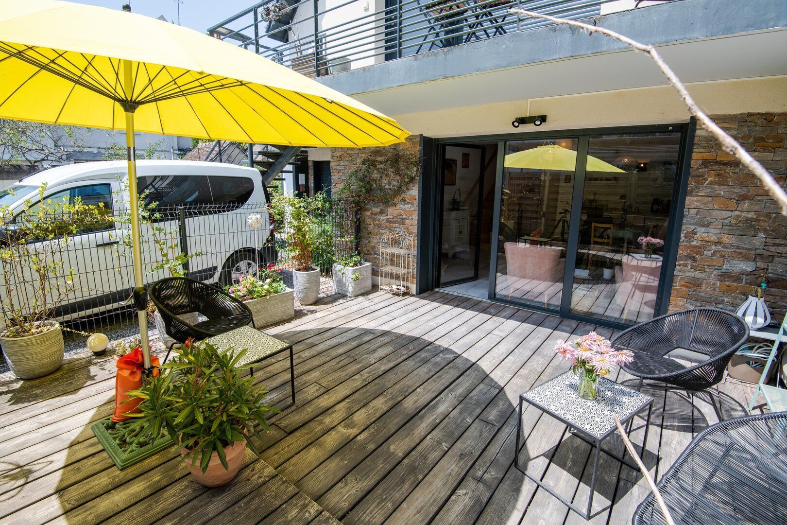 A wooden deck with outdoor furniture, potted plants, and a yellow umbrella.