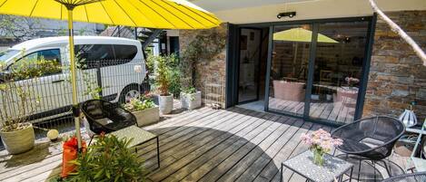 A wooden deck with outdoor furniture, potted plants, and a yellow umbrella.