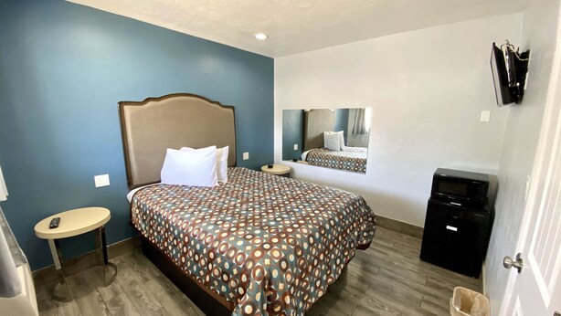 A hotel room with a large bed, a bedside table, a small round table, a trash bin, and a TV on a stand.