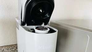 Una macchina per caffè Keurig con una tazza bianca su un piano di lavoro in granito.