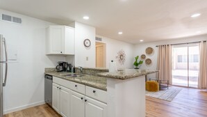 Uma cozinha moderna com armários brancos, bancadas de granito e lava-louças embutida.