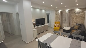 A modern living room with a flat-screen TV, a sofa, a dining table, and a stone accent wall. - NEW Holiday Apartment,A4+2, Family house - OPG Rudan, garden pool, terase, wi-fi (Radonić)