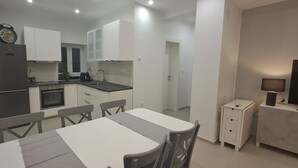 A compact kitchen with white cabinets, a black refrigerator, and a dining area with a table and chairs. - NEW Holiday Apartment,A4+2, Family house - OPG Rudan, garden pool, terase, wi-fi (Radonić)