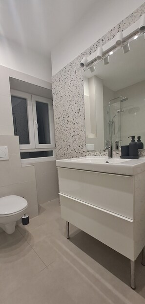 Une salle de bain moderne avec un meuble-lavabo blanc, une cabine de douche en verre et une fenêtre au-dessus des toilettes.
