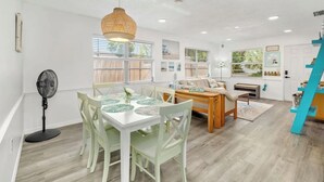 Une pièce lumineuse et bien éclairée, avec une table à manger, des chaises, un ventilateur et un escalier.