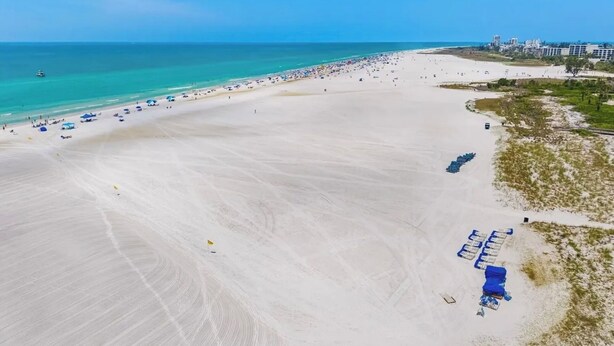 Une vaste plage avec une eau d’un bleu limpide, quelques parasols et une rangée de chaises de plage.