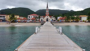 Un muelle de madera que conduce a una iglesia con campanario, rodeado de edificios y palmeras.