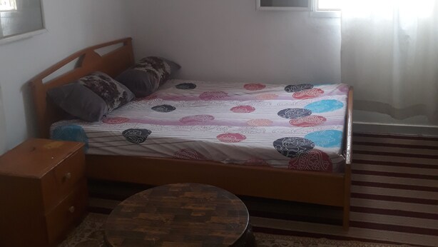 Ein Schlafzimmer mit Bett, kleinem runden Tisch, Fenster mit Vorhängen und einem gemusterten Teppich.