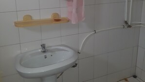 Ein Badezimmer mit einem weißen Waschbecken, einem Holzregal, einem Handtuch auf einem Wäscheständer und einer Duschkabine.