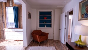 Una stanza con pavimento in legno, una poltrona rossa, una scrivania bianca con una lampada e una libreria blu.